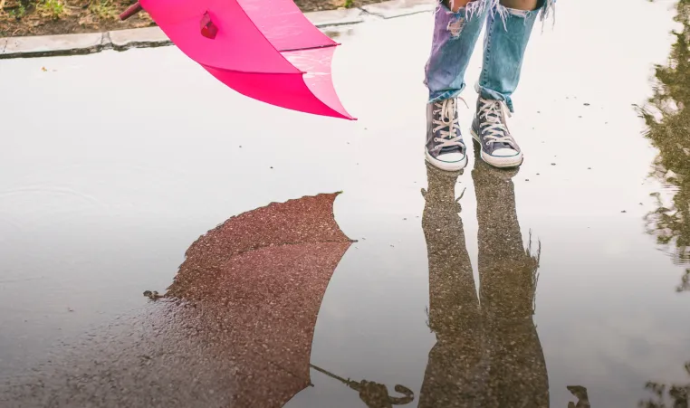 Photo of kids feet jumping in puddle holding pink umbrella